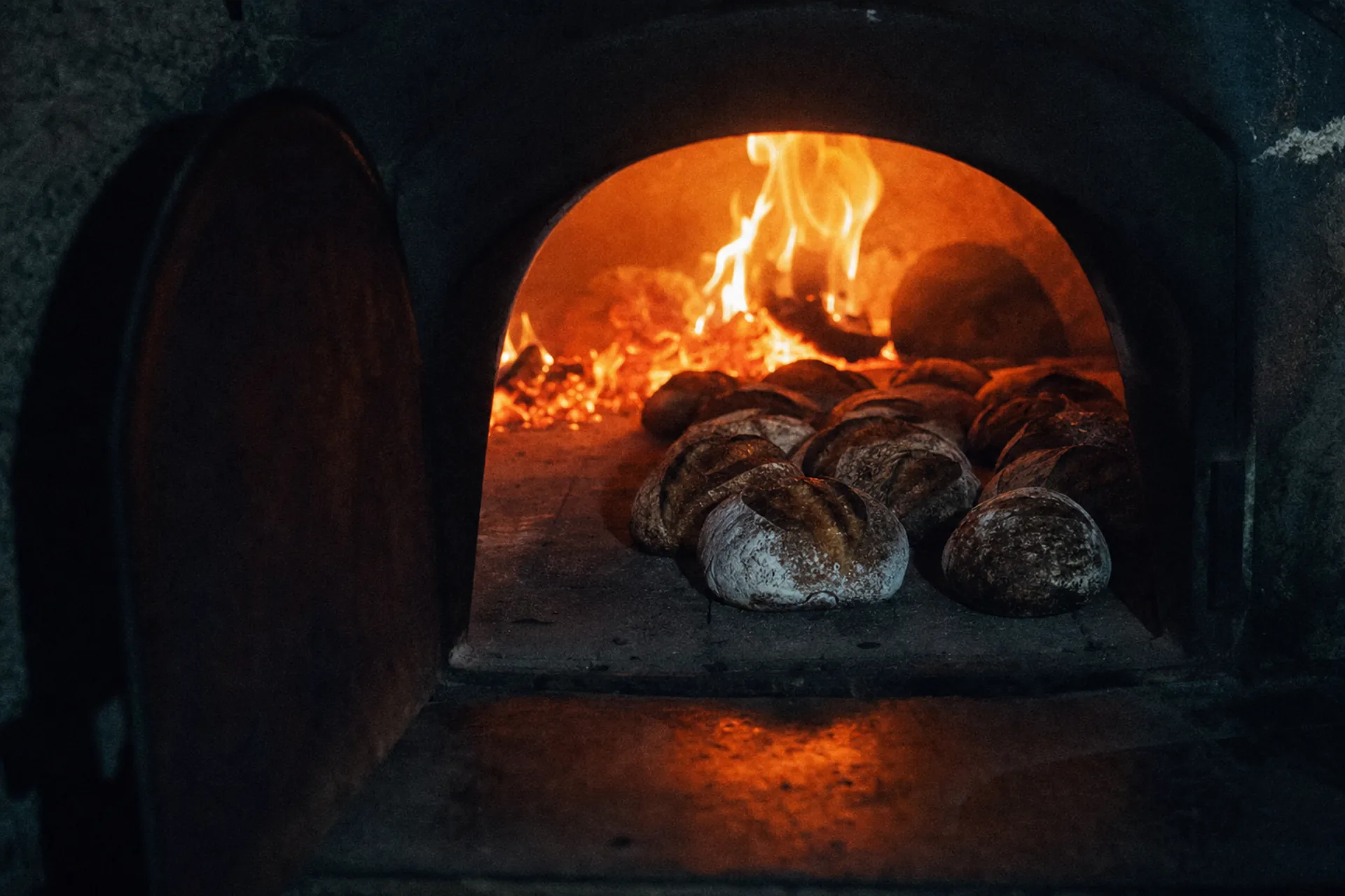 Four à bois ouvert, braises rougeoyantes et miches de pain à croûte foncée sur la sole de pierre.